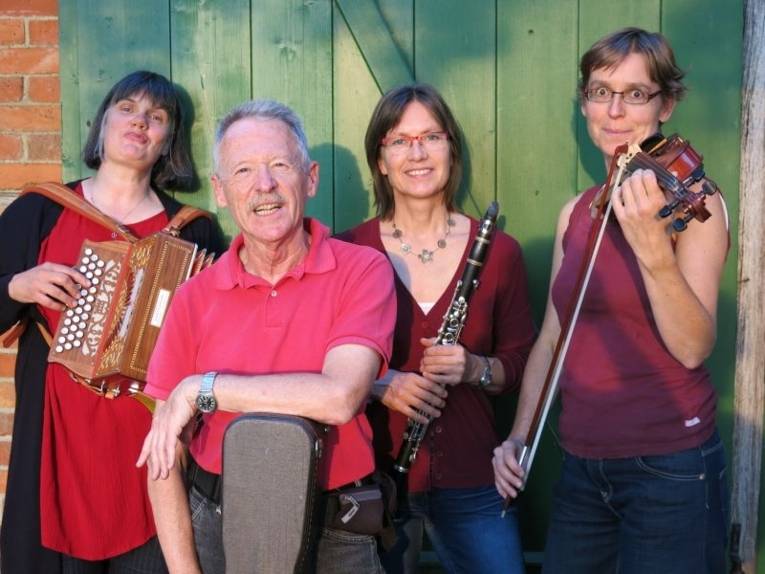 Zu sehen sind drei Musikerinnen und ein Musiker mit Akkordeon, Klarinette, Geige und Gitarre