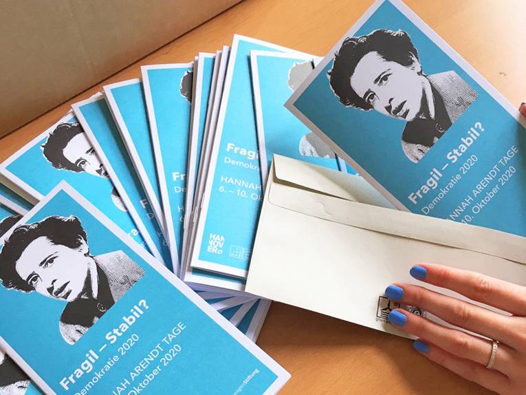 Programmflyer zu den Hannah Arendt Tagen werden von jemandem in Briefumschläge gepackt