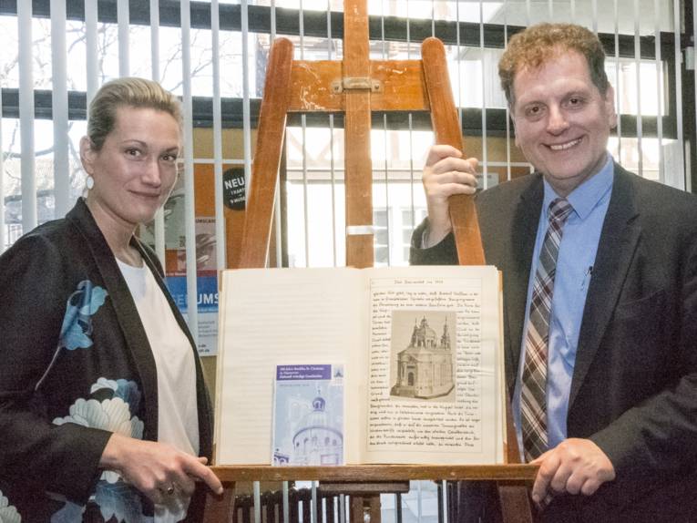 Charlotte Jarosch von Schweder und Dr. Thomas Schwark mit einem Buch über die ST. Clemens-Baslika und dem Programmheft für des Jubiläumsjahr.