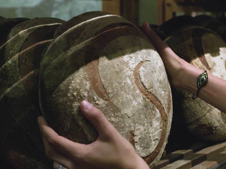 Im Bild zu sehen sind zwei Hände, die Brot aus einem Regal nehmen.