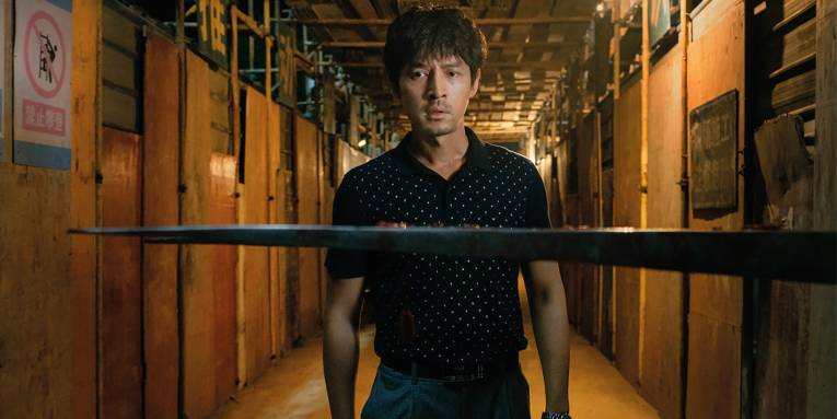 Im Bild zu sehen ist ein Mann vor einer aus der Wand ragenden Klinge.