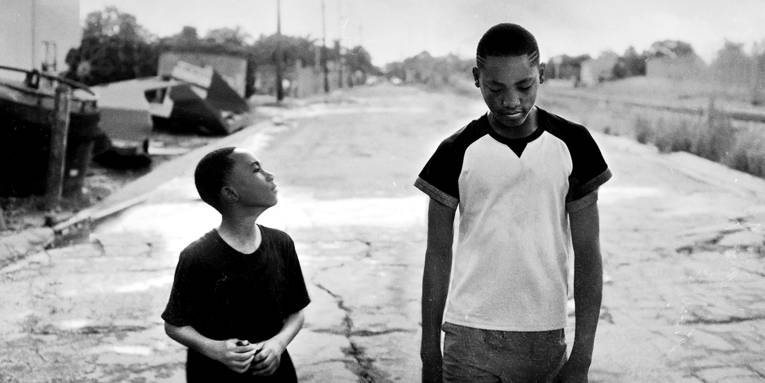 Im Bild zu sehen sind in schwarz weiß zwei dunkelhäutige Kinder auf einer kaputten Straße in einer ärmlichen Gegend.