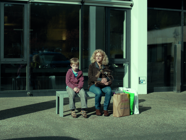 Mutter und Sohn warten auf einer Bank.