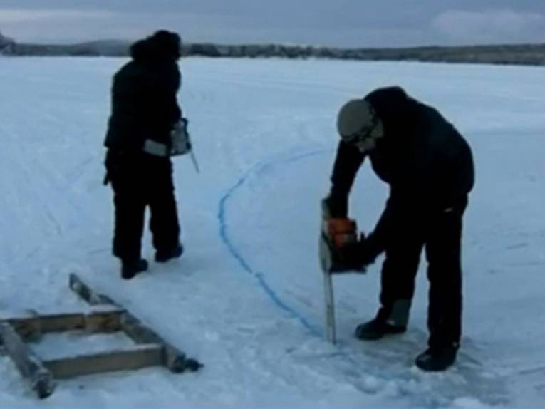 Zwei Männer mit einer Kettensäge auf dem Eis.