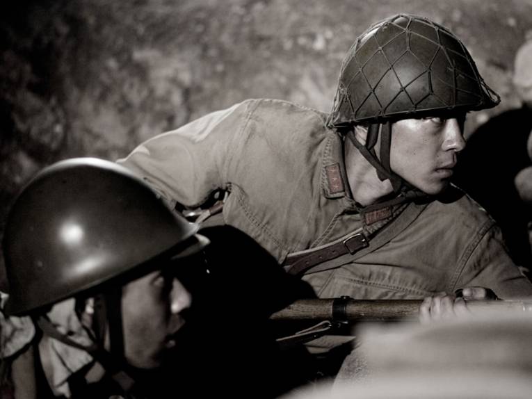 Japanische Soldaten suchen in einem Graben Schutz und spähen nach draußen.