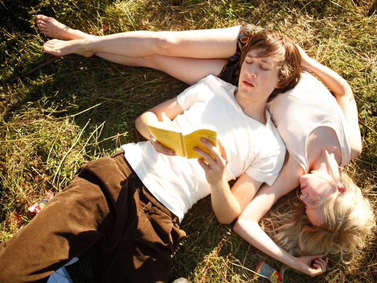 Mann und Frau (Bruder und Schwester) liegen gemeinsam auf einer Wiese und lesen.