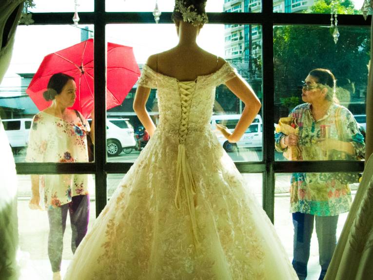 Zu sehen sind zwei Personen, die ein Brautkleid im Schaufenster betrachten.