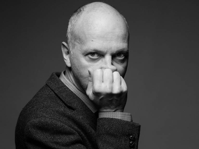 Im Bild zu sehen ist in schwarz-weiß Regisseur Veit Helmer, mit dünnem Bart und Halbglatze. Er stützt seinen Kopf auf sein Handgelenk.