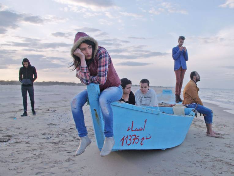 Teenager und junge Erwachsene sitzen auf einem hellblauen Boot am Strand.