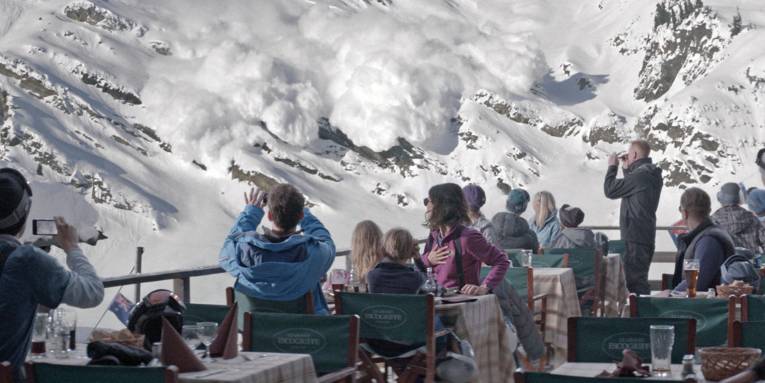 Zu sehen sind mehrere Personen die in einem Restaurant in den bergen eine Lawine beobachten und filmen.