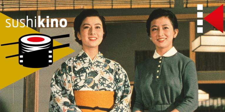 Im Bild zu sehen sind zwei lächelnde Frauen, eine im Kimono, eine im Kleid.