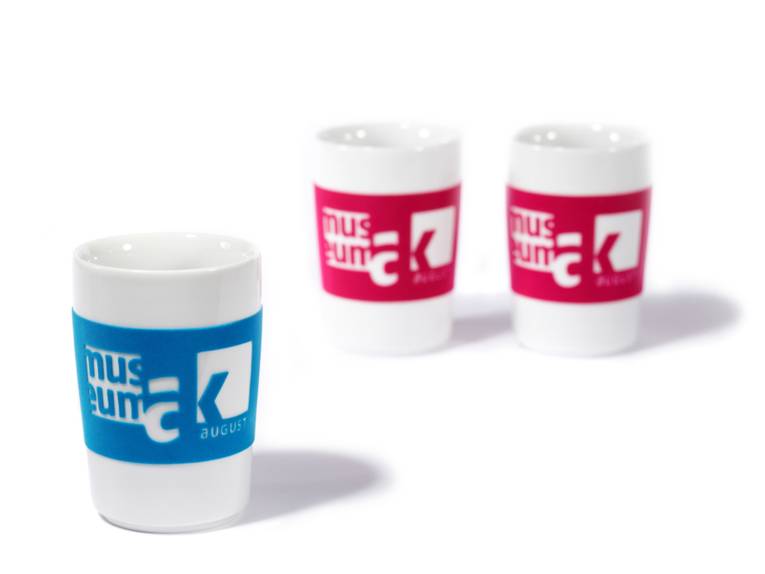 Drei weiße Trinkbecher, die in rot oder blau mit dem Logo des Museum August Kestner bedruckt sind