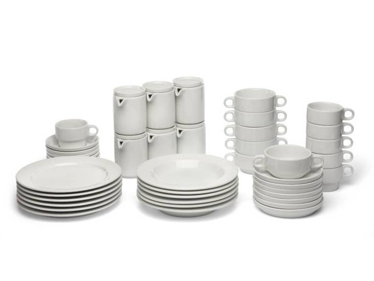 Zahlreiche weiße, gestapelte Teller, Unterteller, Milchkännchen und Tassen vor weißem Hintergrund