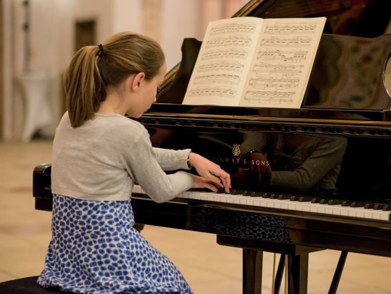 Ein junges Mädchen spielt mit überkreuzten Händen am Klavier.