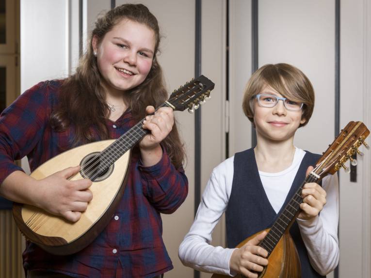 Ein Mädchen mit einer Mandoline, neben einem Jungen mit Mandoline. 