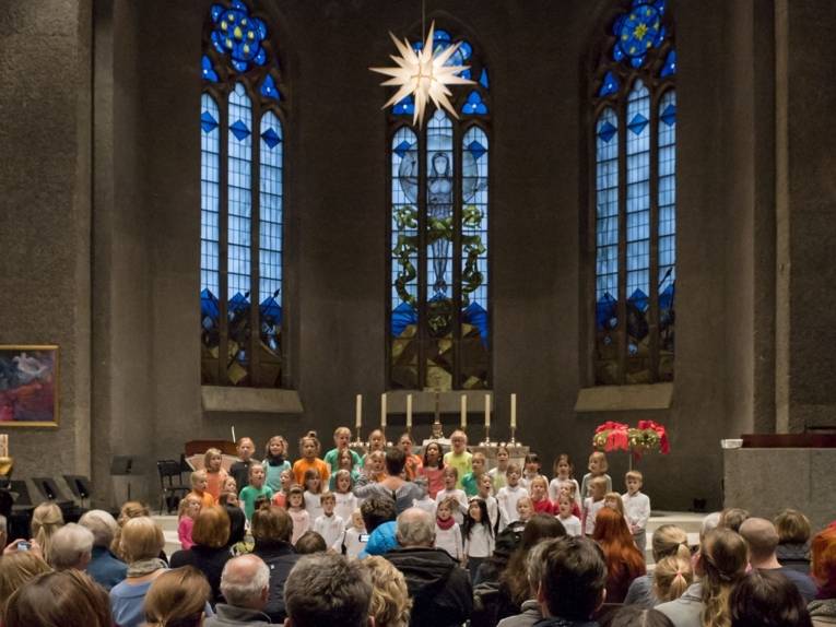 Ein gemischter Chor aus Mädchen und Jungen singt in einer festlich beleuchteten Kirche.