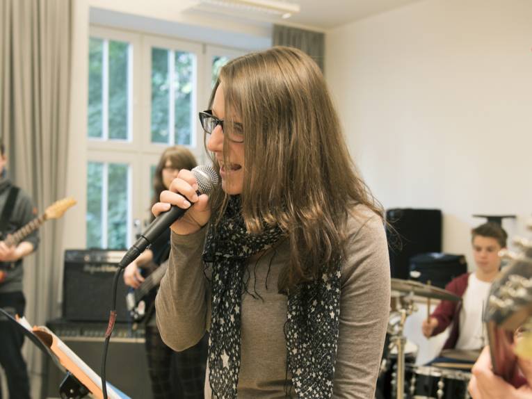 Eine junge Frau mit einem Mikrophon singt, begleitet von einer Band.
