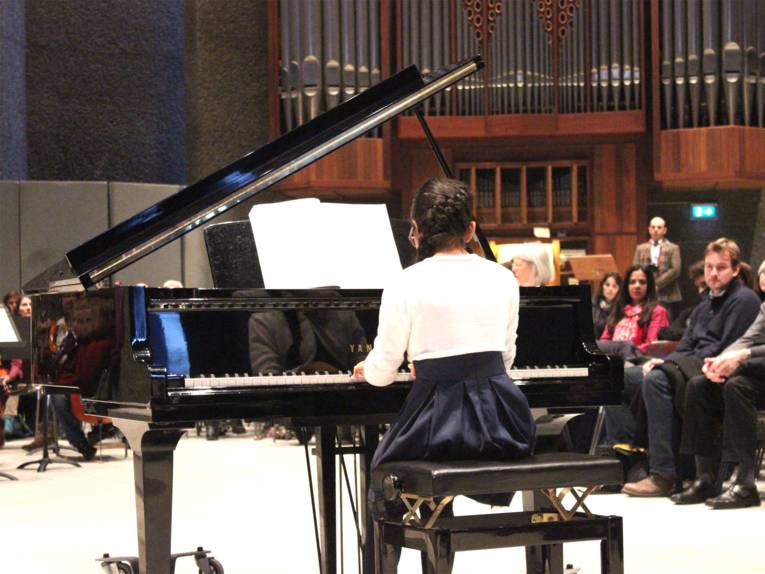 Junge Klavierschülerin am Klavier, im Hintergrund die Orgel und das Publikum