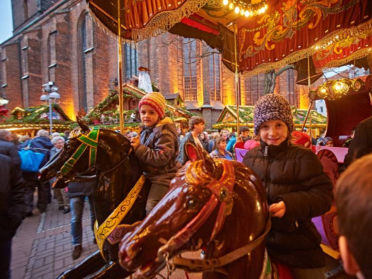 Zwei Mädchen sitzen auf hölzernen Pferden eines historischen Karussells auf dem Weihnachtsmarkt