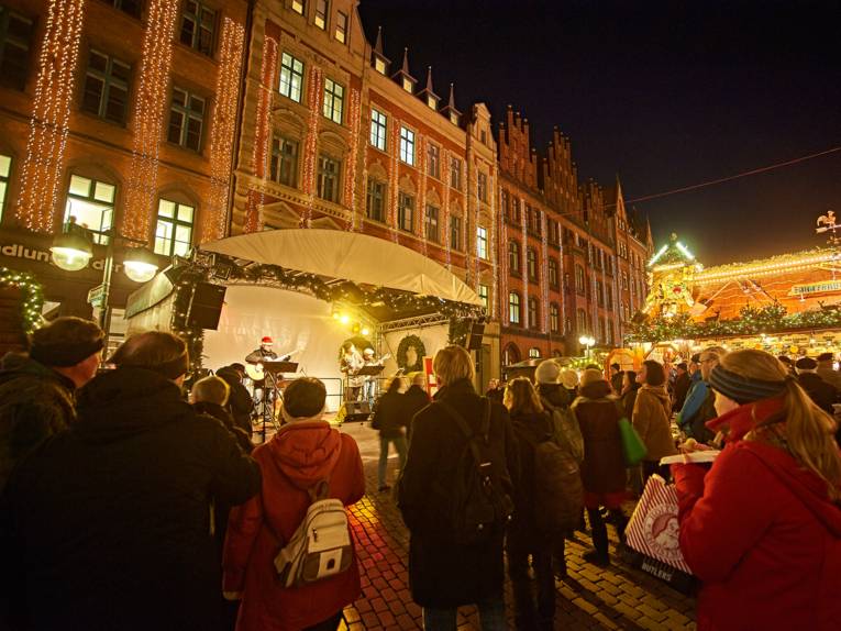 Drei Musiker auf der Bühne, die vor der Buchhandlung an der Marktkirche aufgebaut ist, spielen vor Publikum auf dem Weihnachtsmarkt