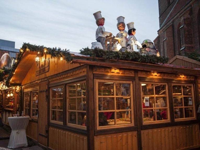 Drei Figuren auf einem Holzdach weisen den Weg zur Weihnachtsbackstube