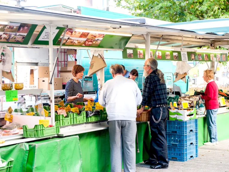 Kunden im Gespräch mit Gemüsehändlerinnen an einem Marktstand