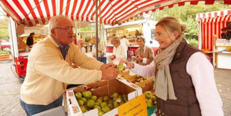 Markthändler gibt Kundin ein Apfelschnitz zum Probieren