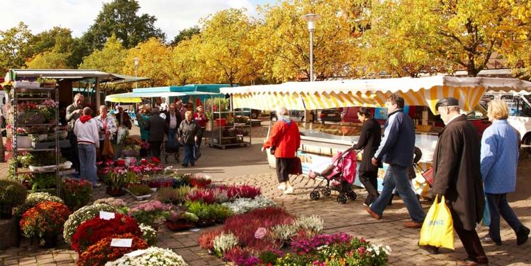 Passanten und Käufer betrachten im Vorbeigehen die Auslagen des Blumenstandes auf dem Sahlkampmarkt