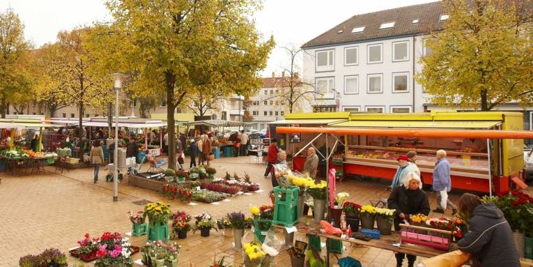Überblick über die verschiedenen Marktstände auf dem Herrenhäuser Markt; im Vordergrund wickelt eine Blumenverkäuferin einen Strauß für eine Kundin ein.