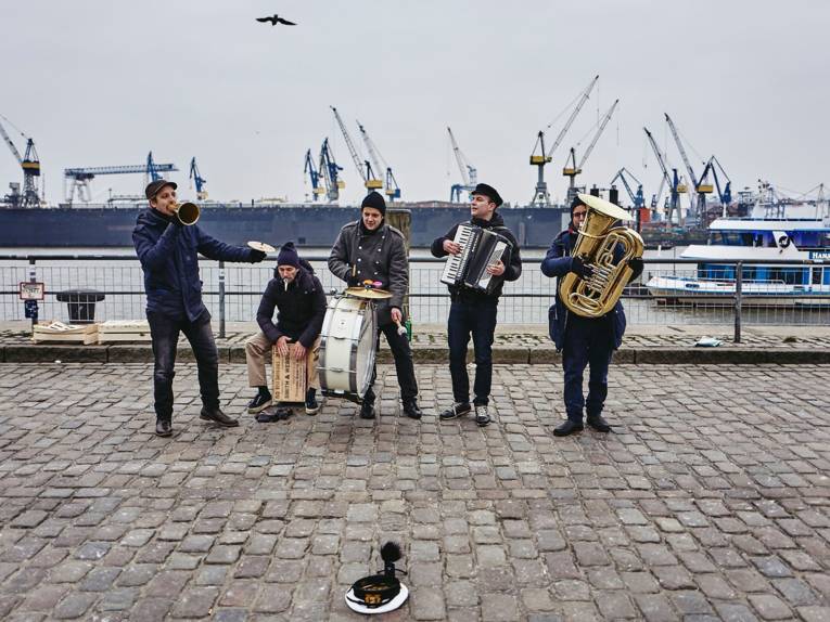 Fünf junge Musiker mit ihren Instrumenten vor Hafenkulisse