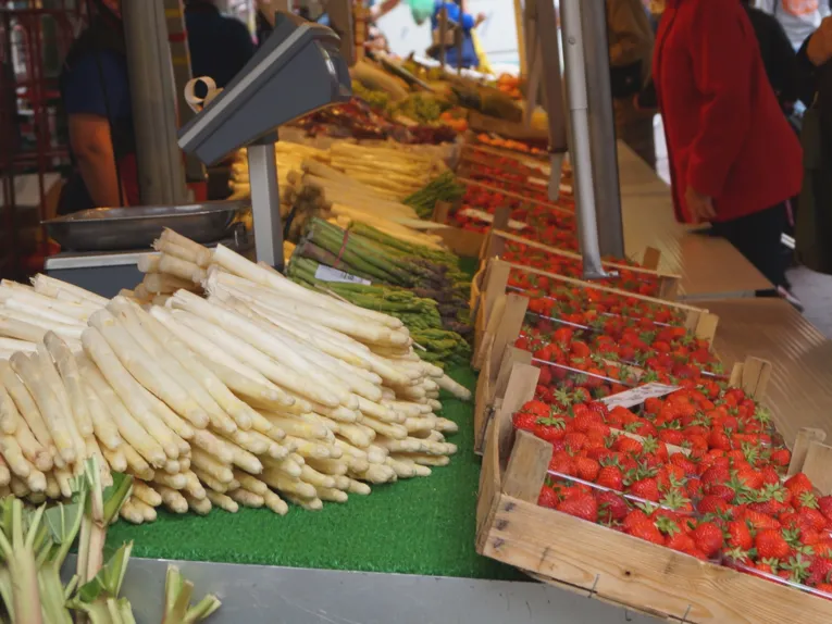 Auf einem Wochenmarktstand liegen Spargelstangen (weiß und grün), Rhabarber und Erdbeeren.