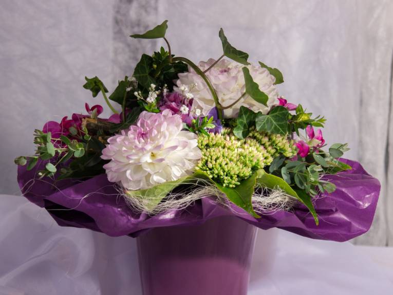 Ein Blumenstrauß mit weißen Dahlien, Sedum, Efeu und rosa Alpenveilchen