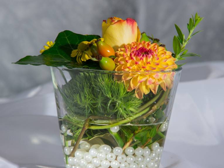 In einem Wasserglas liegen auf Glasperlen und Wasser Blumenblüten