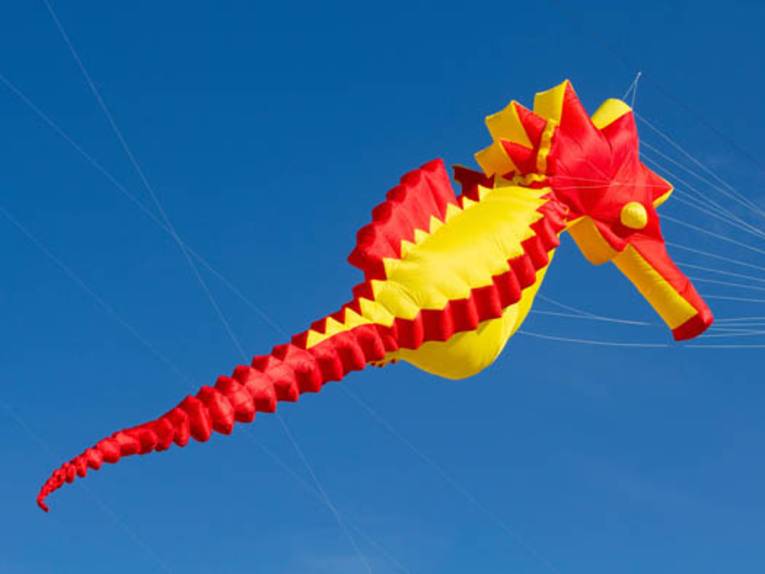 Gelb-roter Lenkdrachen in Form eines Seepferdchens vor blauem Himmel