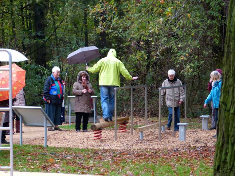 Eine Person mit Regenschirm balanciert auf einem Holzstamm im Bewegungspark in Stöcken
