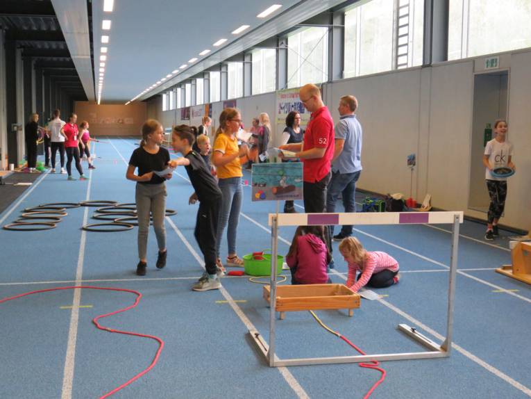 Kinder und Jugendliche an Sportständen in einer Halle. 