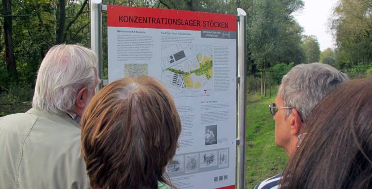 Teilnehmer einer Fahrradtour betrachten die Informationstafel zum KZ Stöcken, 2014