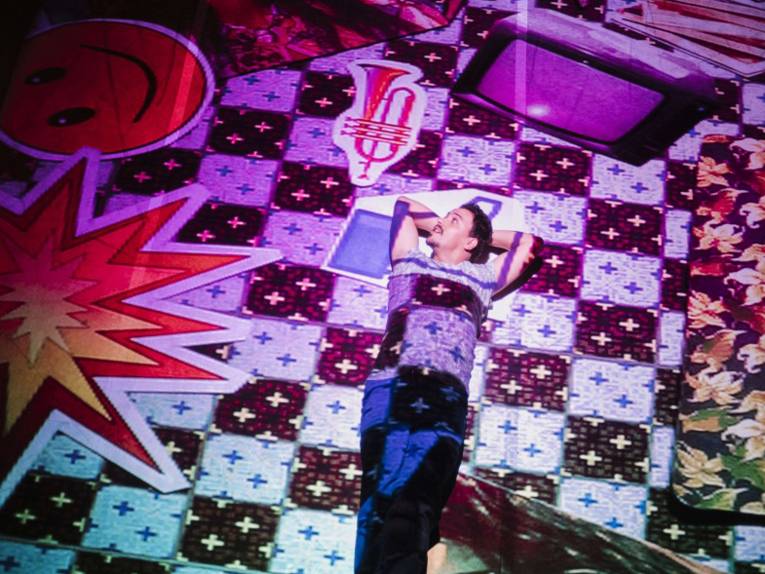 Auf dem Boden liegender Mann. Der Boden wird lilafarben angestrahlt. 