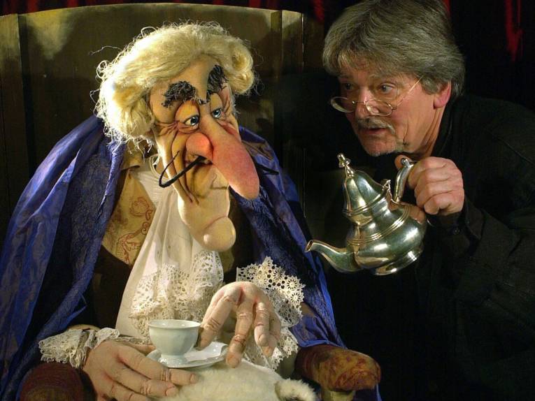 Eine Tee trinkende Puppe und ein Mann, der ihr einschenkt. 