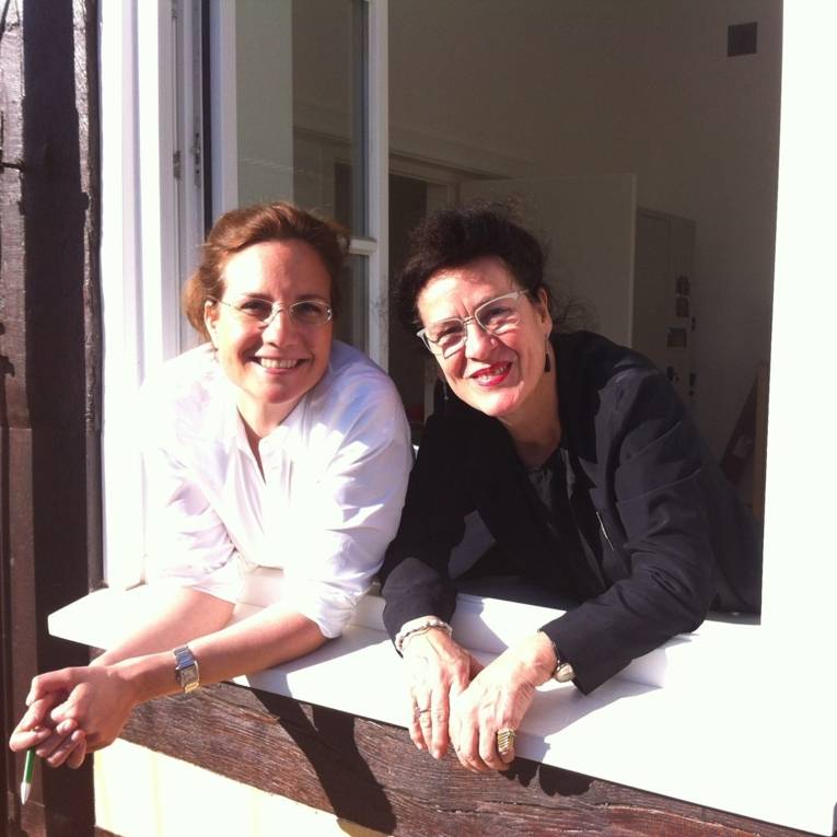 Inga Samii und Elisabeth Schweeger lehnen sich aus einem Fenster im Erdgeschoss und lachen in die Kamera