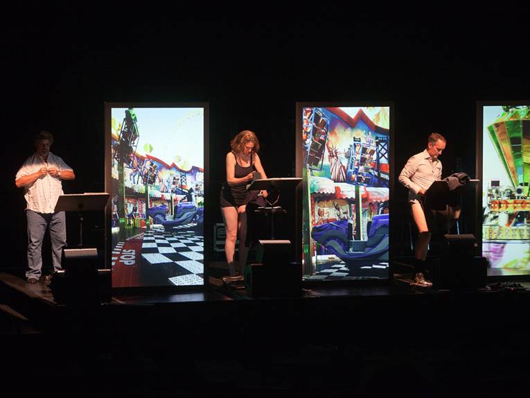 Drei Sänger auf einer Bühne neben drei Videoleinwänden.