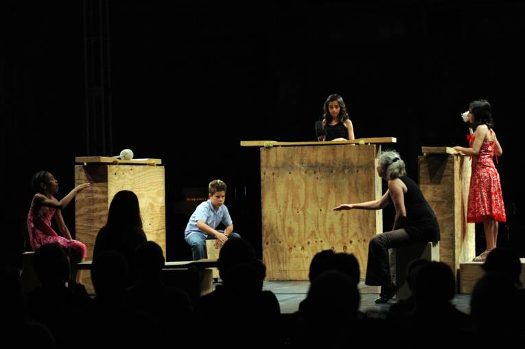 Blick auf eine Bühne; vier Kinder trommeln auf Holzkästen