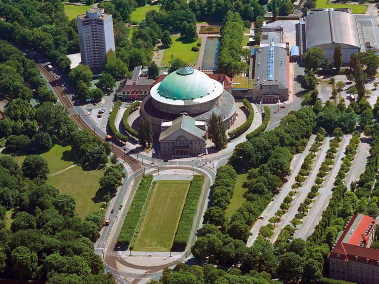 Luftaufnahme des Hannover Congress Centrums im Sommer; um das auffällige Kuppelgebäude herum tragen alle Bäume ein dichtes Blattwerk
