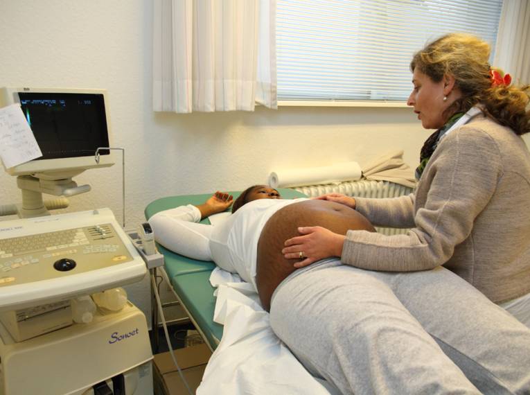 Eine schwangere Frau liegt auf einer Behandlungspritsche, eine Ärztin tastet den Bauch ab