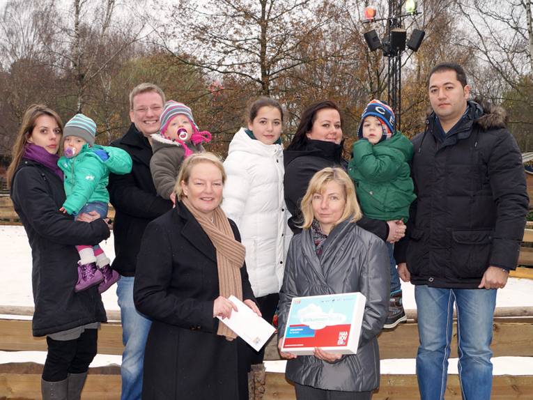 Zwei Familien mit Kindern, davor zwei Frauen, die ein Willkommenspaket in den Händen halten