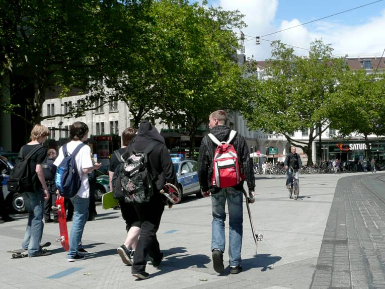 Eine Gruppe Jugendlicher, teilweise mit dem Skateboard unterwegs, auf dem Bahnhofsvorplatz