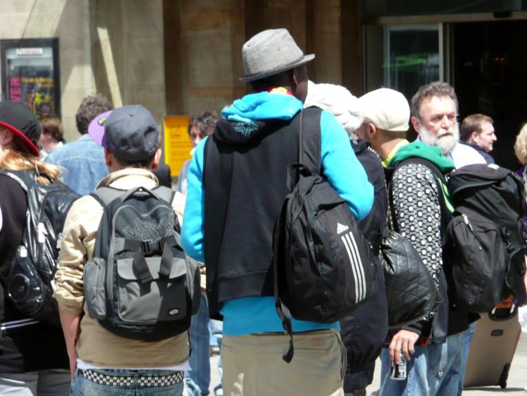 Zwei Jugendliche stehen, mit dem Rücken der Kamera zugewandt, vorm Hauptbahnhof in Hannover. Um sie herum einige weitere Personen.