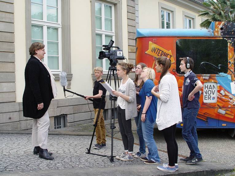 Eine Frau wird vor der Kamera von einer Gruppe Jugendlicher interviewt