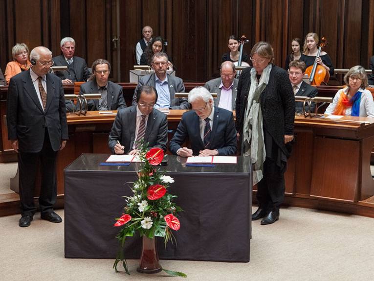 An einem Tisch im Hodlersaal des Neuen Rathauses sitzen Bürgermeister Kazumi Matsui aus Hiroshima und Bürgermeister Bernd Strauch aus Hannover und unterzeichnen ein Memorandum, das den Willen zur zukünftigen Zusammenarbeit der beiden Städte unterstreicht