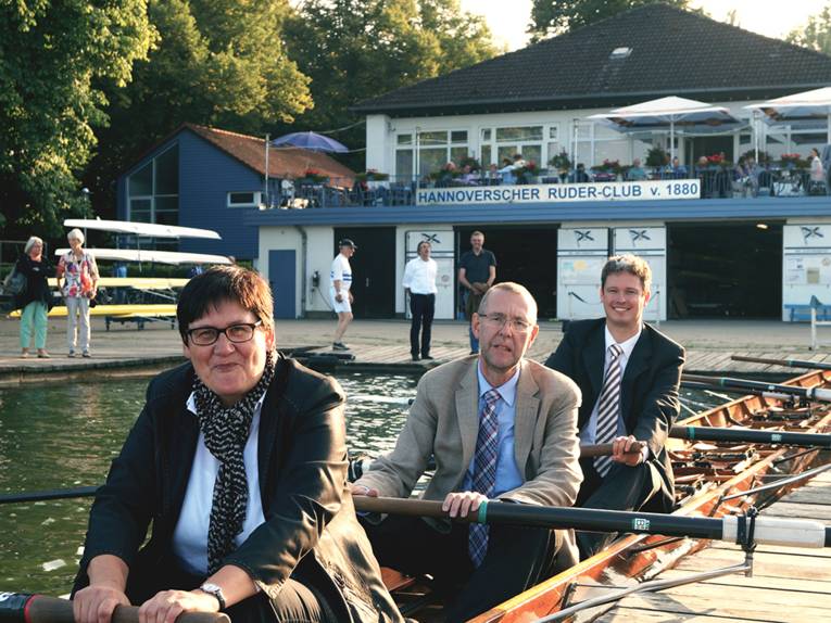Sabine Tegtmeyer-Dette, Prof. Dr. Axel Priebs und Prof. Dr. Timm Eichenberg in einem Ruderboot, im Hintergrund das Vereinshaus des HRC